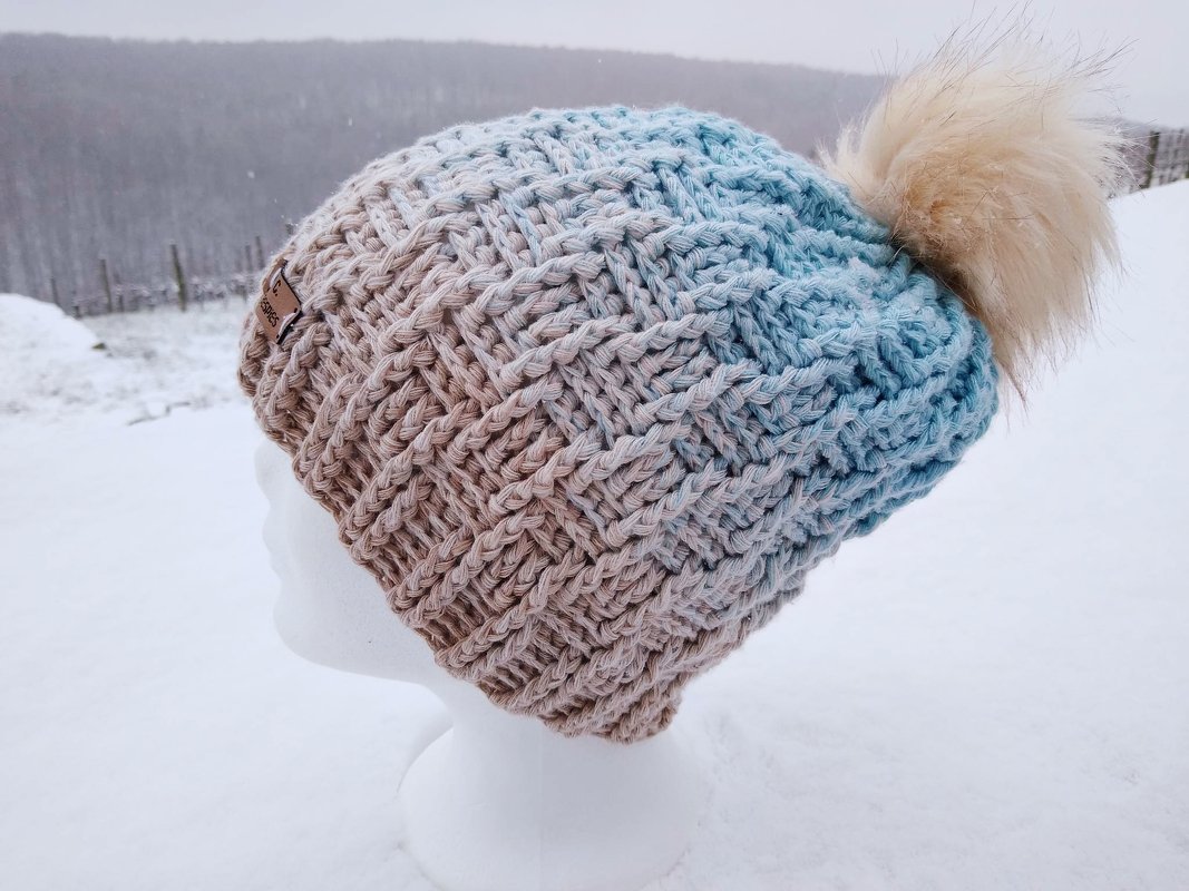 Gehäkelte Mütze in Beige zu Blau im Ombre mit Flechtmuster und hellem Bommel auf Mannequinkopf im Schnee