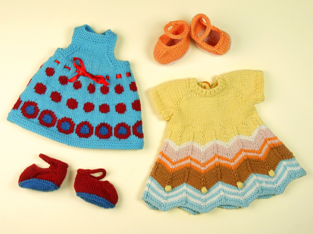 Hand-knitted doll dresses and two pairs of tiny knitted shoes on a light background.