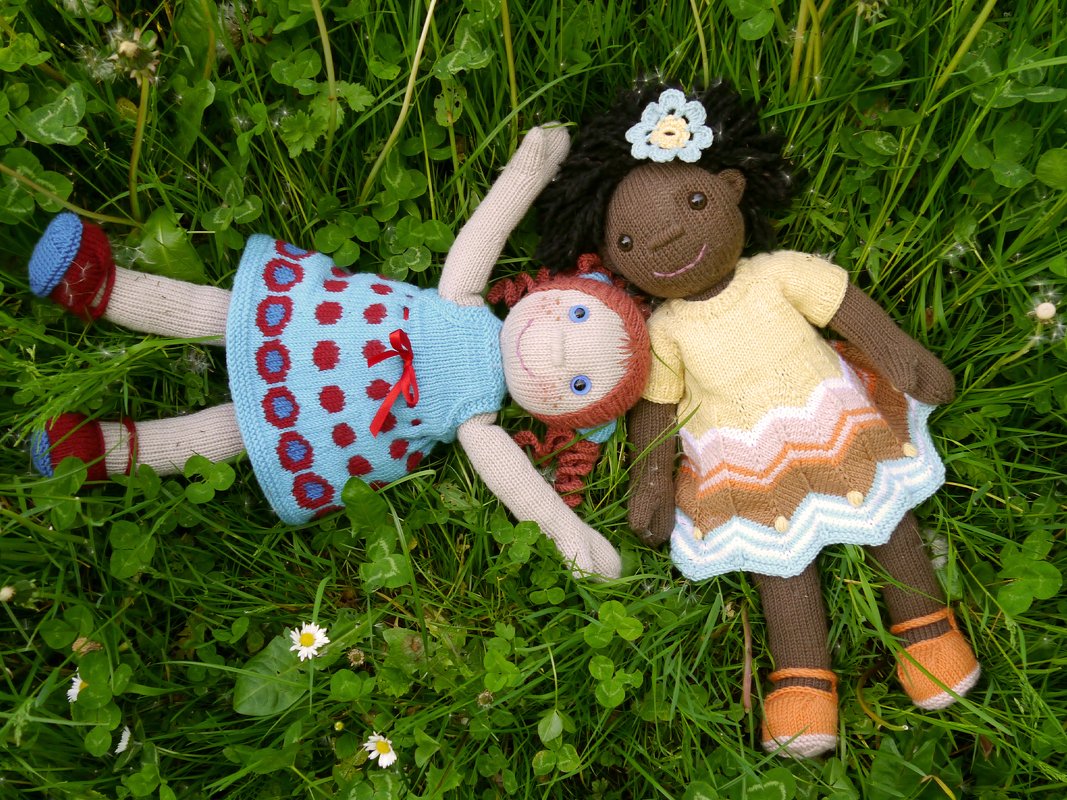 Two knitted dolls in colorful patterned dresses lying on grass with daisies