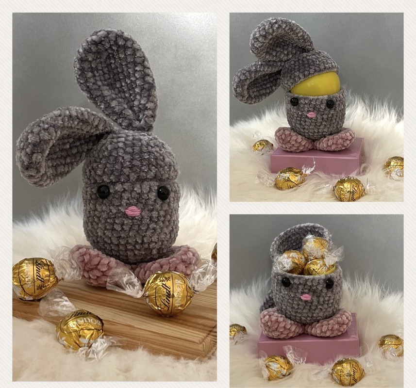 Graues, gehäkeltes Amigurumi-Häschen mit rosa Pfötchen und Nase auf flauschigem Untergrund, geeignet als Osterversteck.