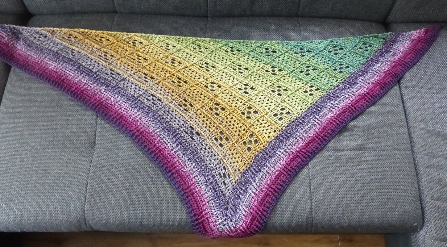 Gehäkeltes Dreieckstuch in Magenta, Gelb und Grün mit Lochmuster auf grauem Sofa