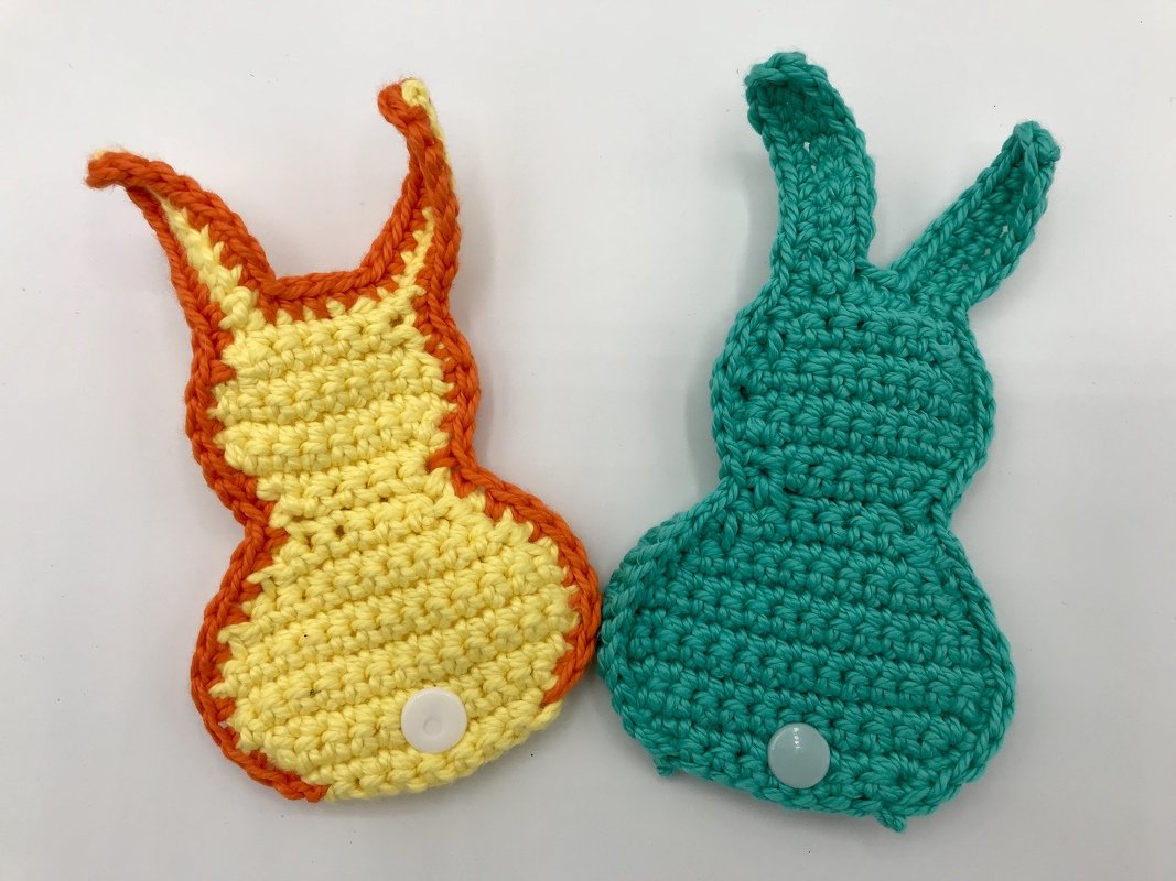 Zwei gehäkelte Hasenapplikationen, gelb-orange und türkis, jeweils mit kleinem Knopf als Schwanz