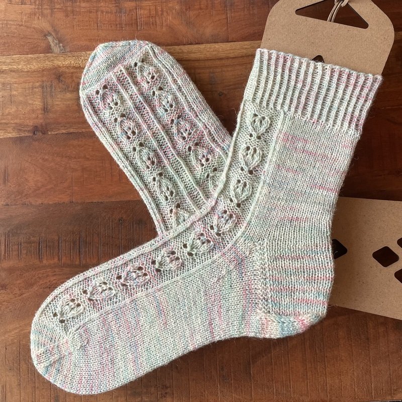 Ein Paar hell gestrickter Damensocken mit Lochmuster, liegend auf einer Holzoberfläche.