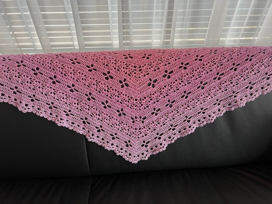 Rosa gehäkeltes Dreieckstuch mit Loch- und Blütenmuster über schwarzem Sofa drapiert