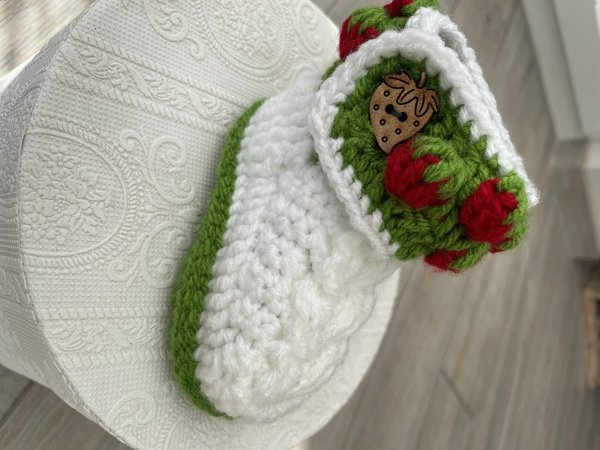 Gehäkelter weißer Babyschuh mit grünem Rand, roten Erdbeeren und kleinem Holzknopf
