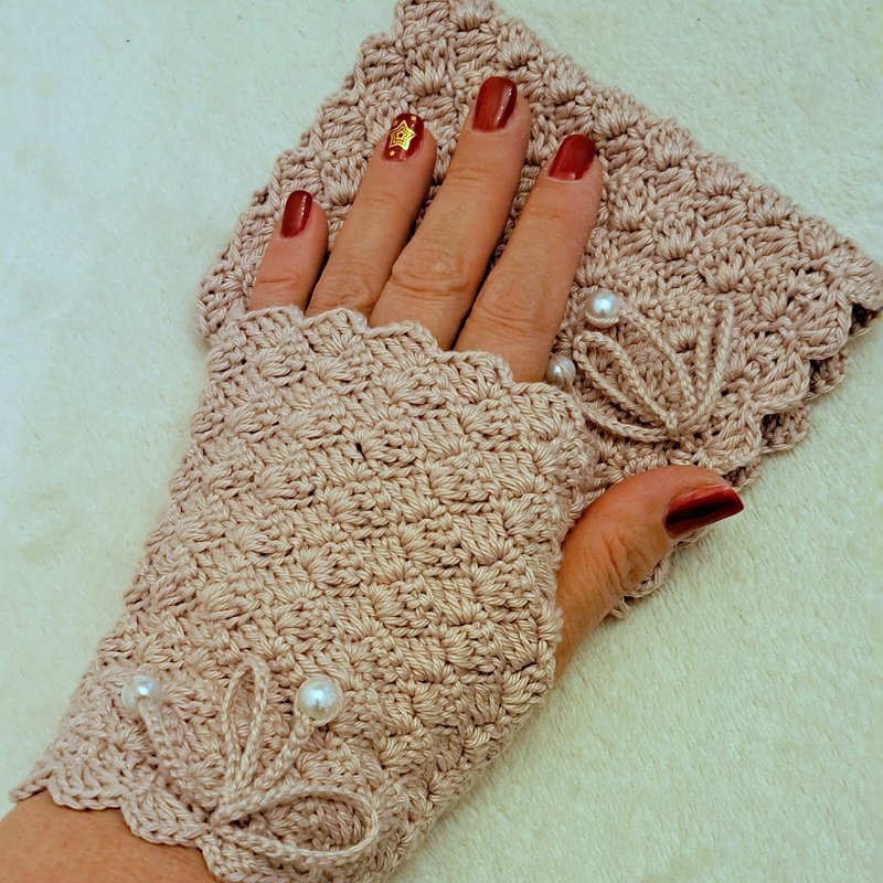 Hand mit gehäkelter fingerloser Stulpe in hellem Rosé mit Muschelmuster und Perlen