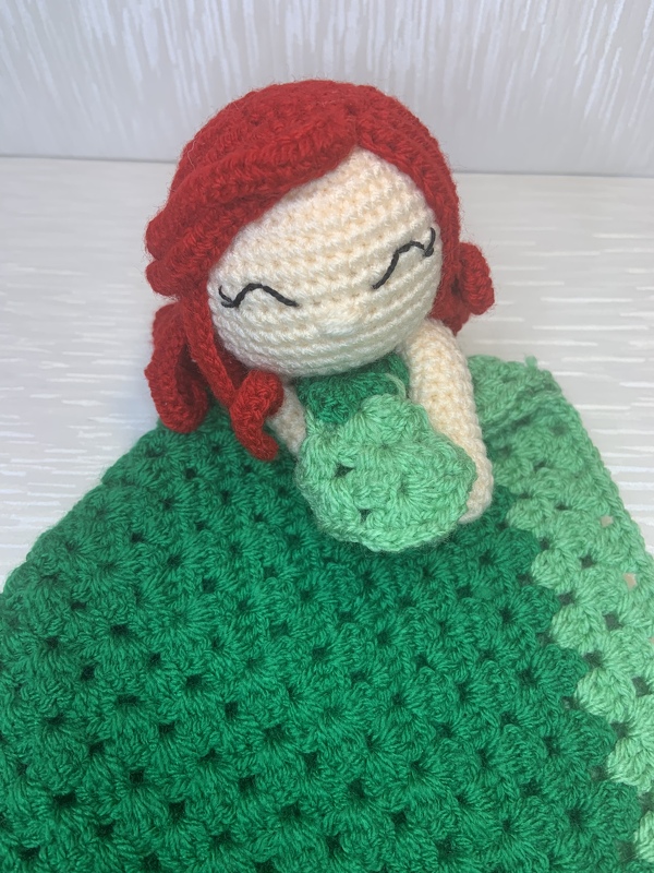 Crocheted lovey: red-haired amigurumi doll attached to green granny-stitch blanket