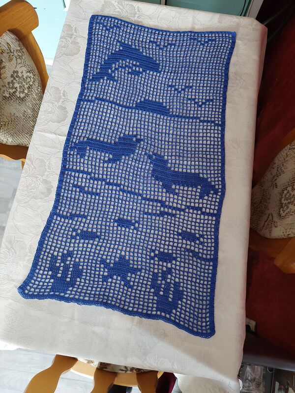 Blauer gehäkelter Tischläufer mit Delfin- und Fischmotiven auf weißem Tischtuch