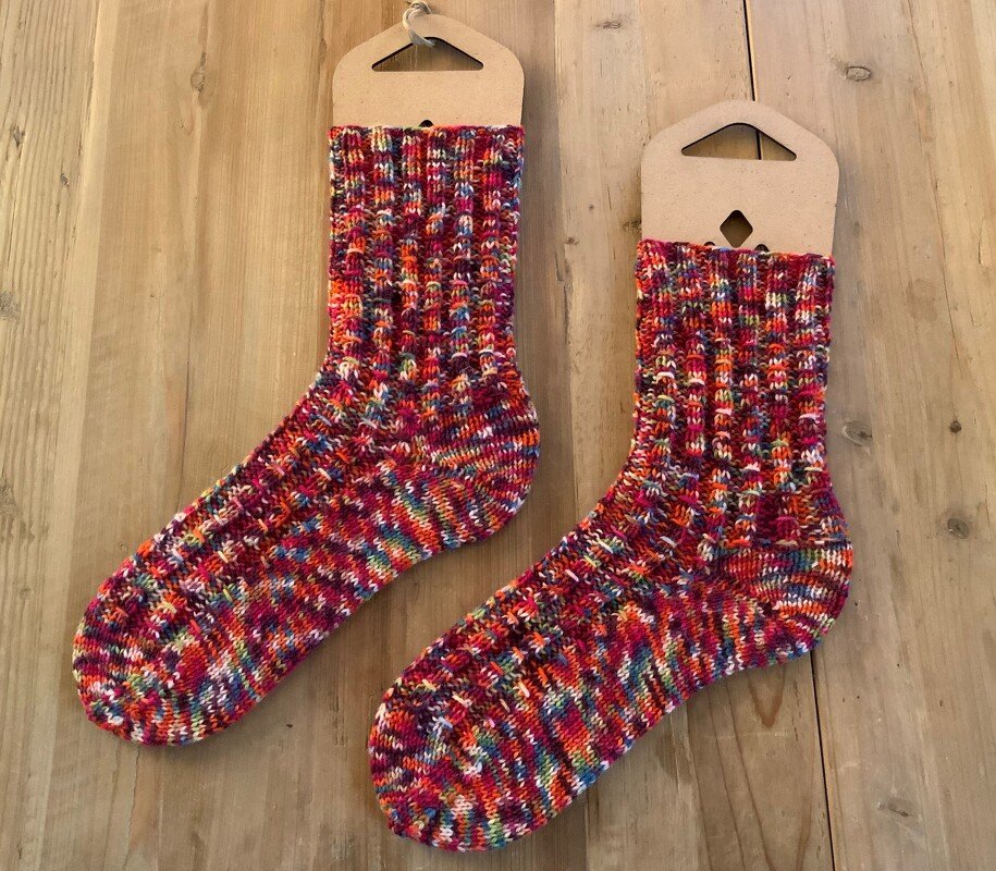 Mehrfarbige handgestrickte Socken mit Rippenbündchen auf Kartonaufhängern vor Holz
