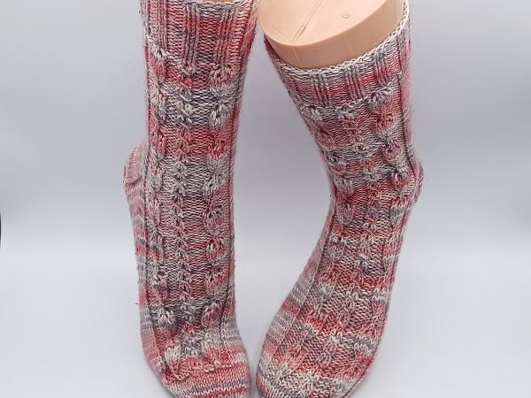 Paar grau-rote Stricksocken mit Rippen- und Zopfmuster auf Modellfüßen