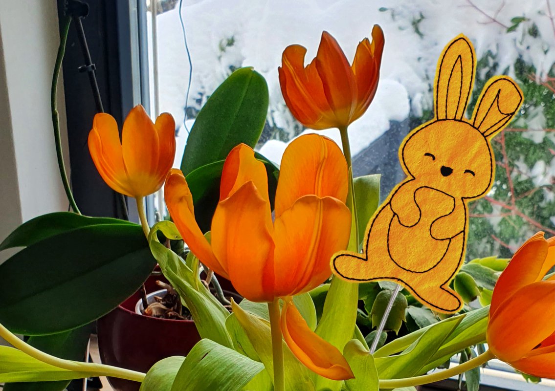 Gestickter orangefarbener Osterhase als Pflanzenstecker zwischen Tulpen