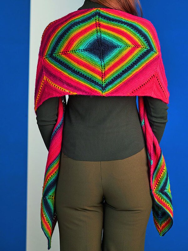 Rückenansicht einer Person mit gestricktem Dreiecksschal mit zentraler Regenbogen-Raute und pinken Seitenrändern