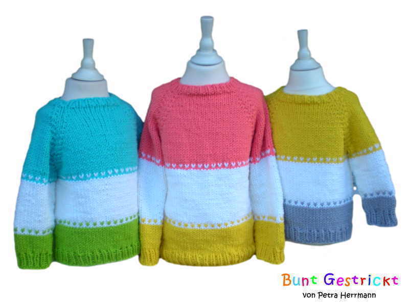 Drei gestrickte Kinderpullover auf Schaufensterpuppen in Türkis‑Grün, Rosa‑Gelb und Gelb‑Grau mit weißem Mittelstreifen