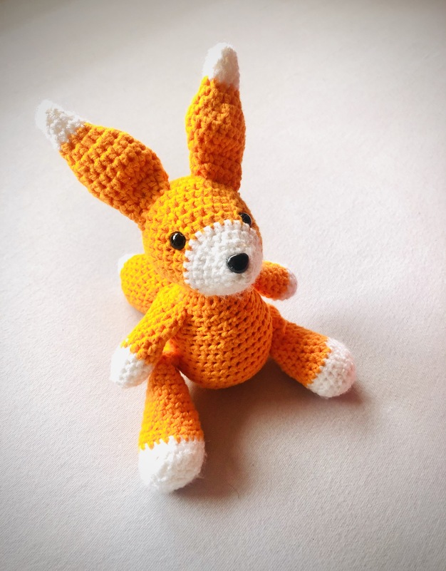 Gehäkelter Amigurumi-Fuchs in Orange und Weiß mit langen Ohren und weißen Pfoten