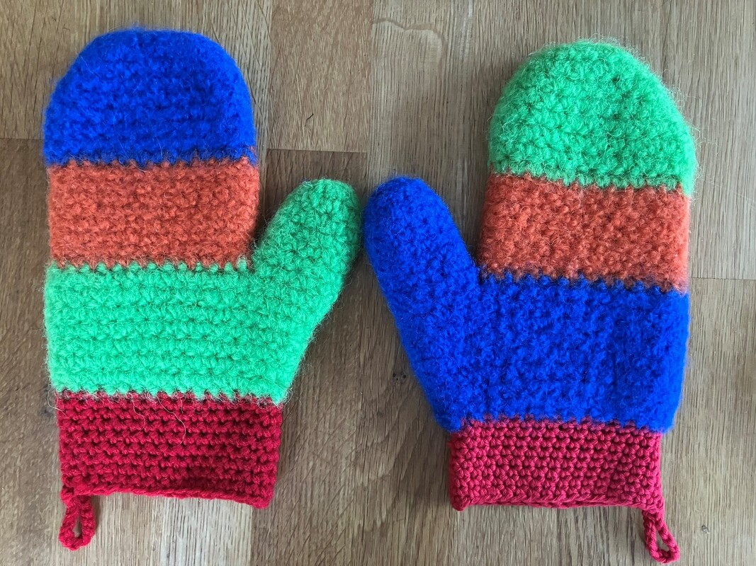 Gehäkelte gestreifte Ofenhandschuhe in Blau, Grün, Orange und Rot auf Holz