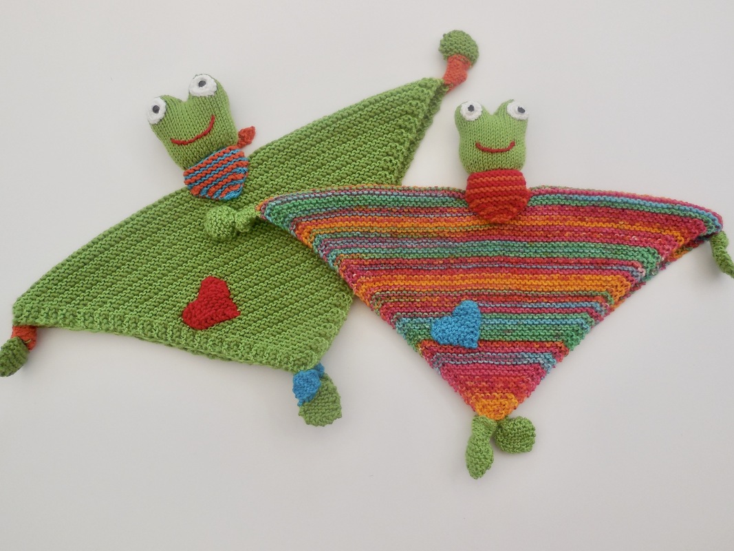 Zwei gestrickte dreieckige Schmusetücher mit Froschköpfen, eines grün, eines bunt gestreift, mit Herz-Applikationen und Knoten an den Ecken