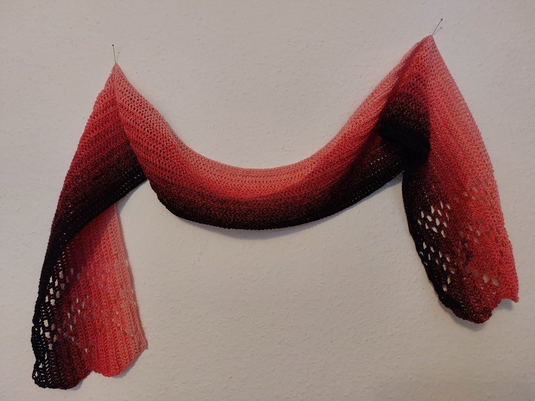 Gehäkelter länglicher Schal mit Koralle-zu-Dunkelrot-Verlauf, an einer Wand befestigt, Spitzenmuster an den Enden