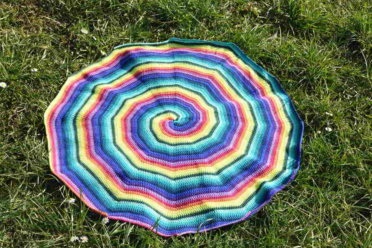 Bunte spiralförmige Häkeldecke in Regenbogenfarben auf Gras