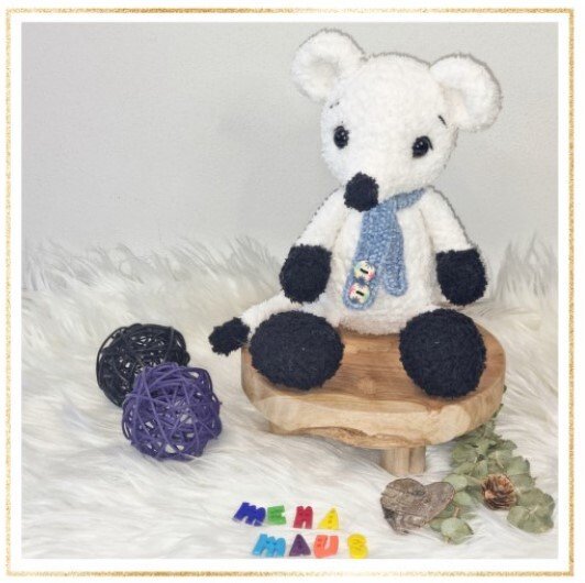 Weiß-schwarze gehäkelte Amigurumi-Maus mit blauem Schal auf Holzpodest