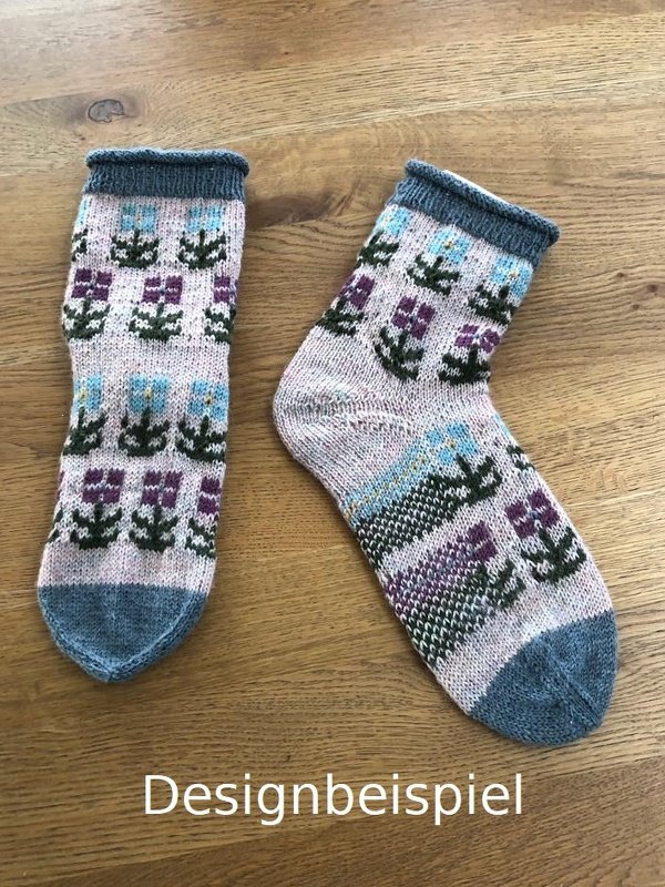Zwei gestrickte Socken mit Blumenmuster in Rosa, Lila und Hellblau auf Holzuntergrund.