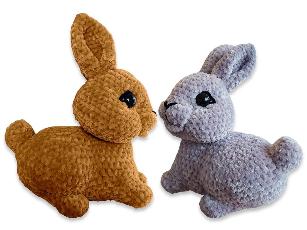 Two plush amigurumi crochet bunnies, one brown and one lilac, facing each other on a white background.