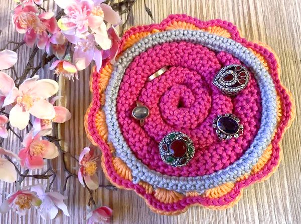 Gehäkelte runde Blütenschale in Pink, Grau und Orange mit Ringen und Blütenzweig auf Holz