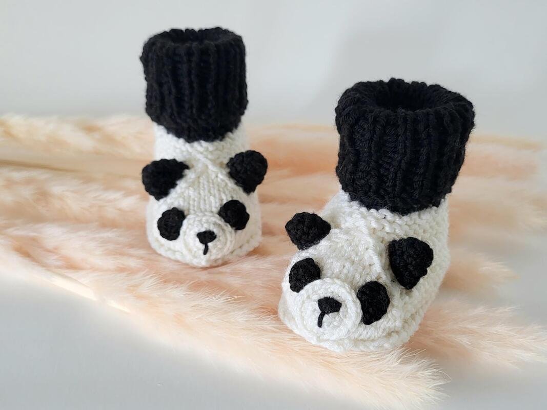 Paar gestrickte Panda-Babyschuhe auf hellem, weichem Hintergrund
