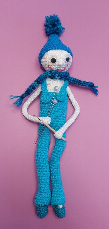 Gehäkelte Amigurumi-Puppe in blauem Outfit mit Mütze, Schal und Nadeln
