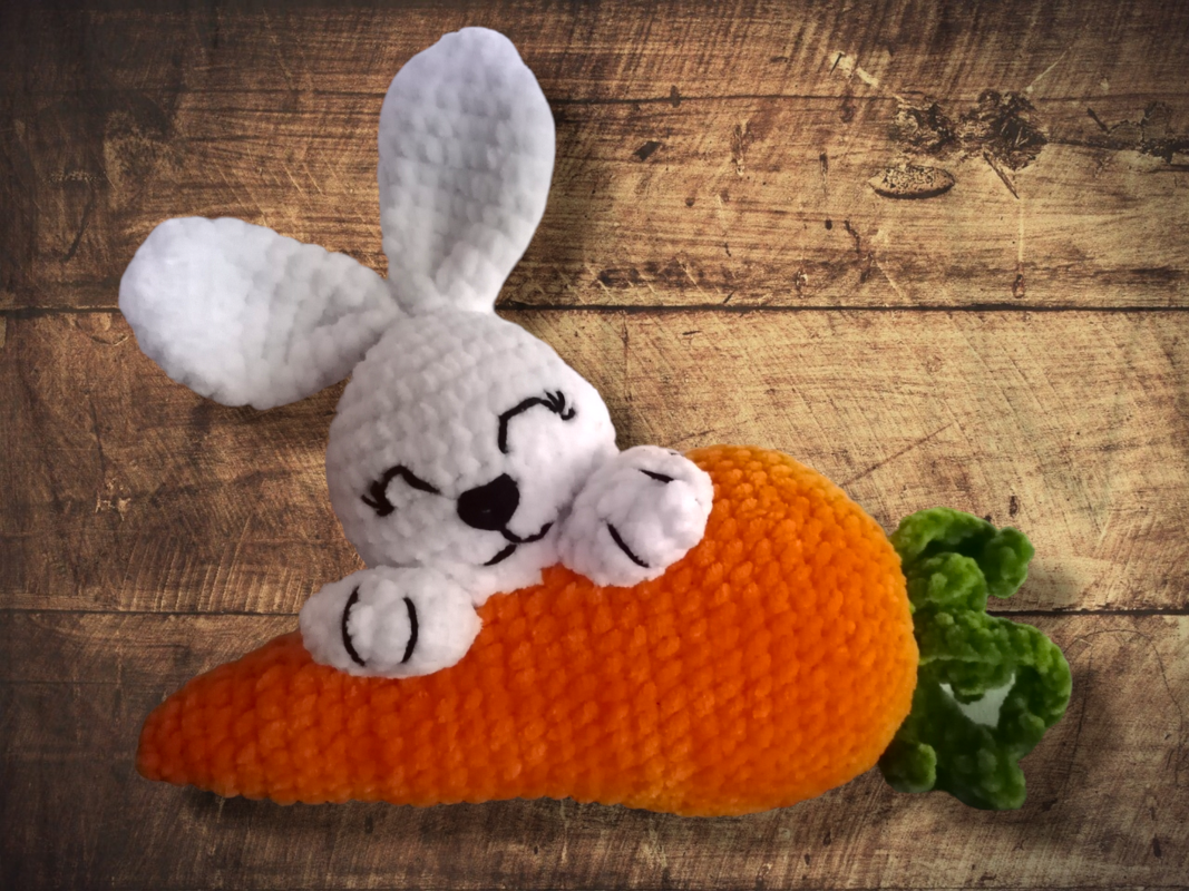 Lächelnder weißer Amigurumi-Hase, liegend auf oranger Karotte