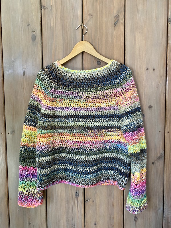 Multicolor striped crochet crewneck sweater hanging on a wooden hanger