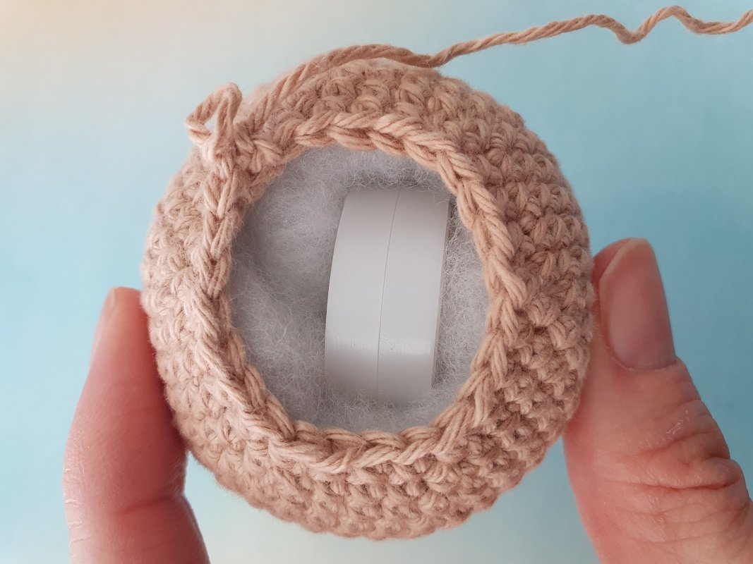 Hand holding crocheted rattle cover revealing fiber stuffing and a plastic inner ring