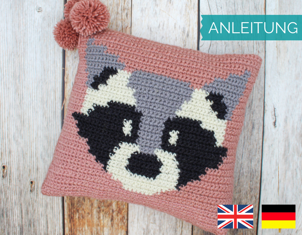 Rosa gehäkelter Kissenbezug mit stilisiertem Waschbärgesicht und Bommel