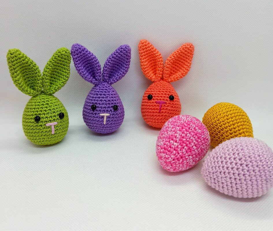 Three colorful amigurumi bunnies and three crocheted eggs arranged on a white surface