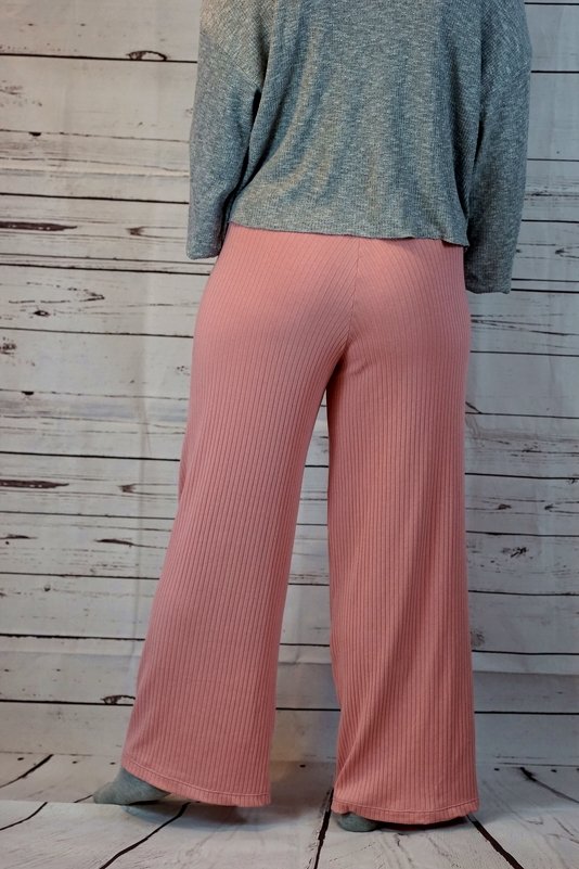 Rückansicht einer Person in weiter, gerippter rosa Hose vor einer Holzplankenwand