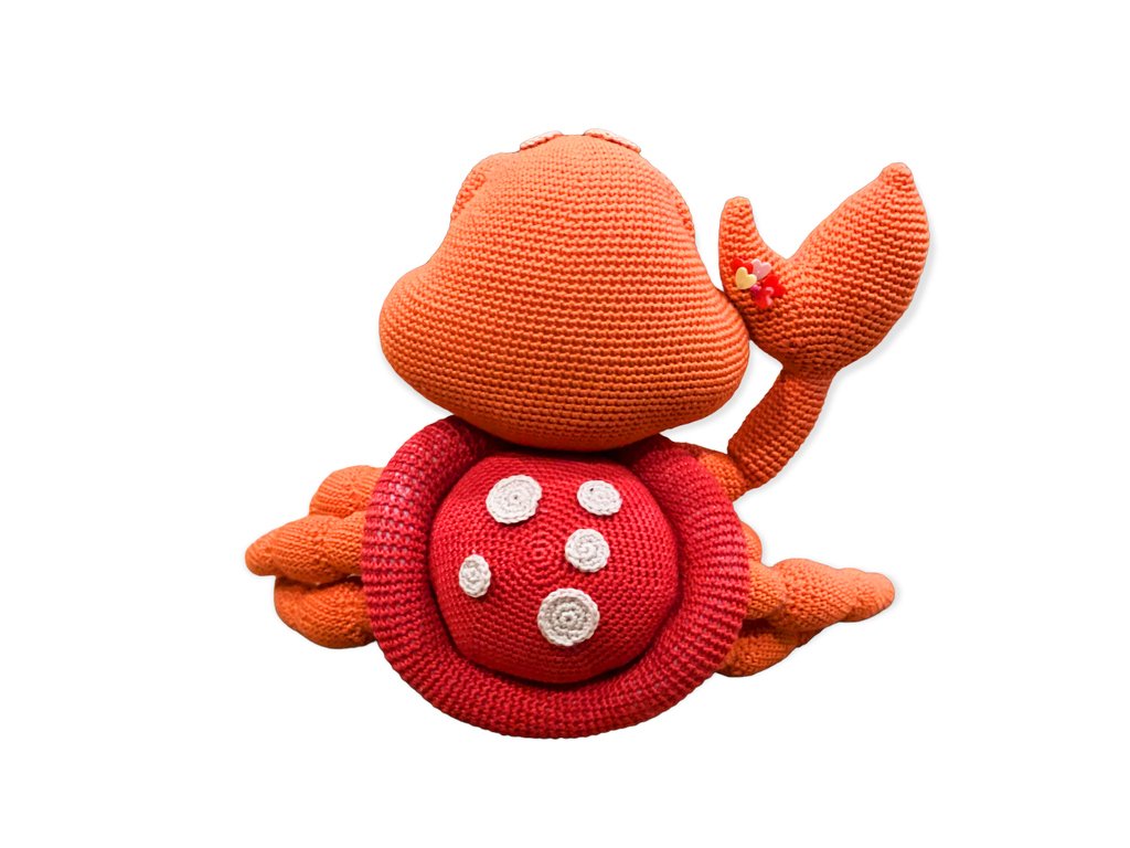 Gehäkelter Amigurumi-Krebs in Rot und Orange mit weißen Punkten und Blüte an der Kralle vor weißem Hintergrund