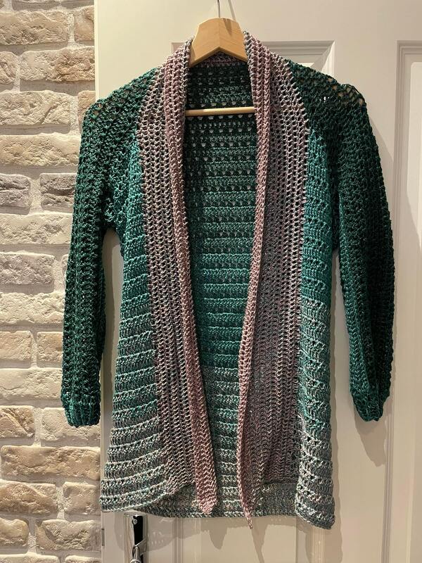 Gehäkelte offene Damenjacke mit Farbverlauf in Grün- und Rosétönen an einem Bügel