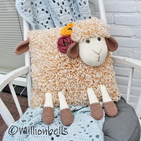 Crocheted sheep pillow with textured cream loop-stitch body, brown ears and hooves, and two small crocheted flowers.