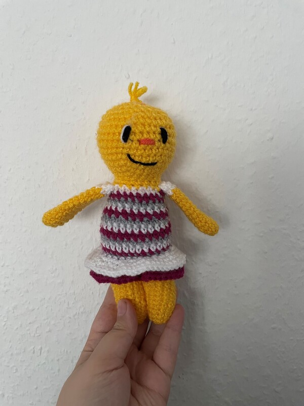 Gehäkeltes gelbes Amigurumi-Küken im gestreiften Kleid, in der Hand gehalten