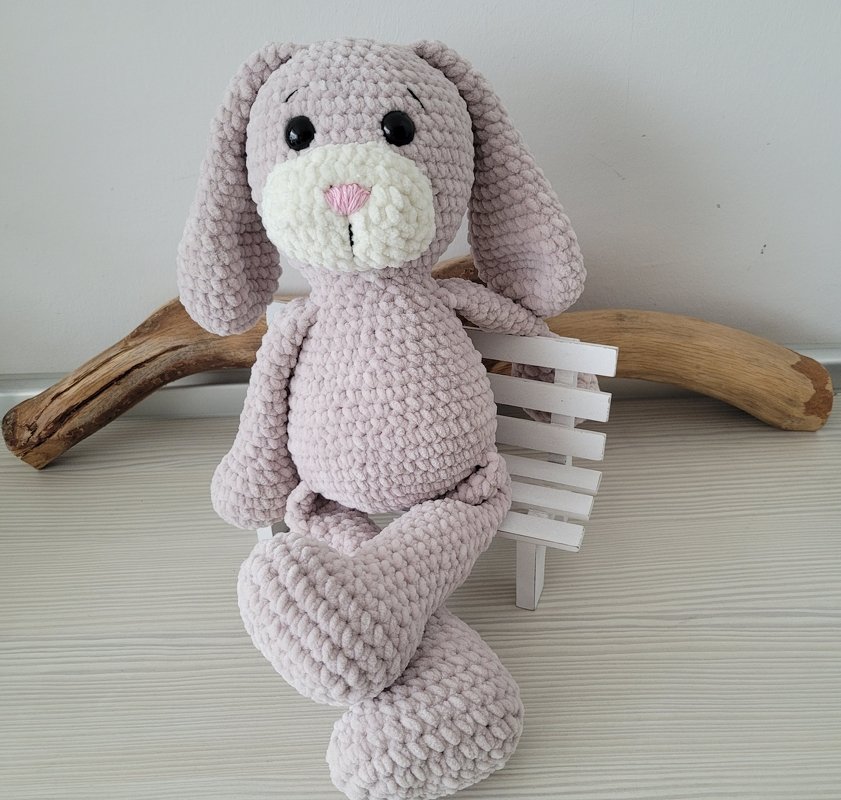 Zartrosa gehäkelter Amigurumi‑Hase aus flauschigem Chenille‑Garn auf weißer Miniaturbank