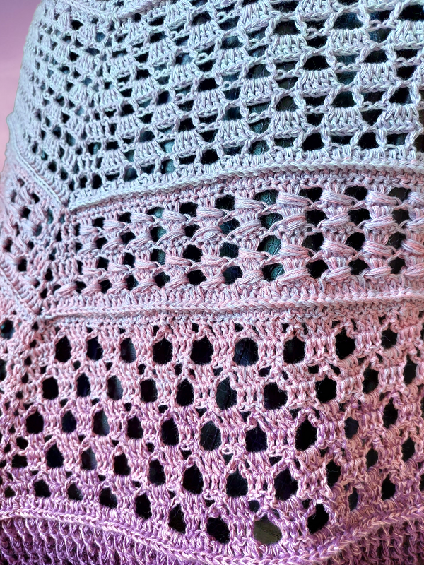 Detailed view of openwork and textured stitches on a lavender and pink gradient triangle crochet shawl.