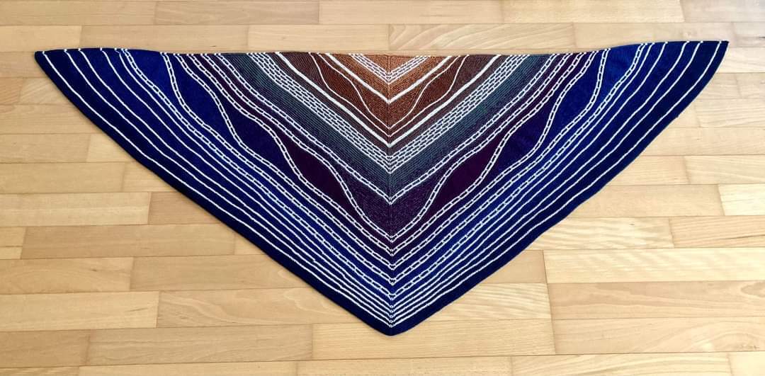 Gestricktes Dreieckstuch in Blau, Braun und Weiß mit Streifen- und Wellenmuster auf Holzboden