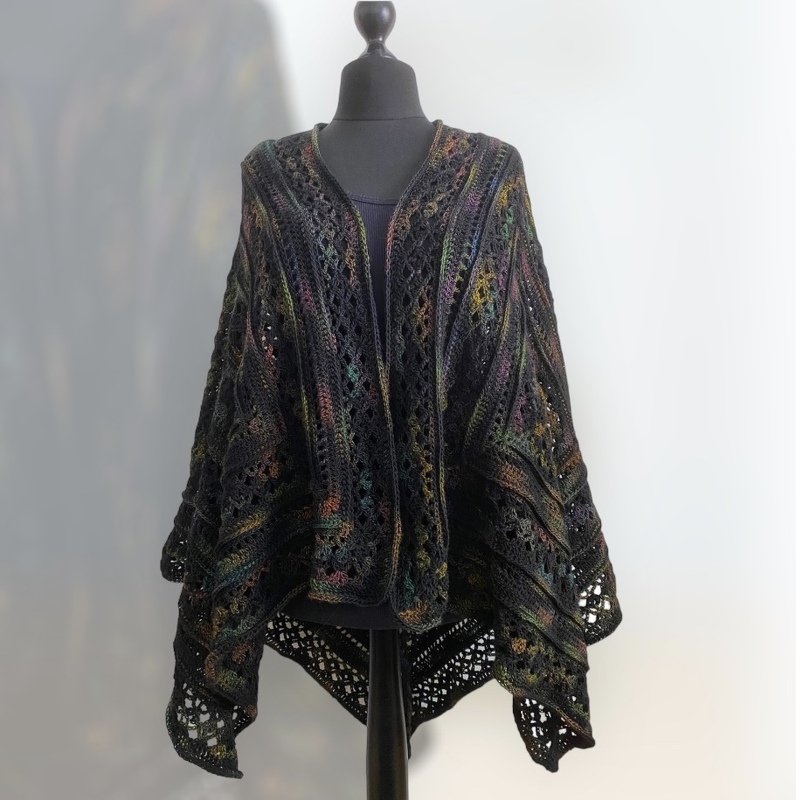 Dark crocheted shawl with openwork lace panels and subtle multicolor flecks on a mannequin.