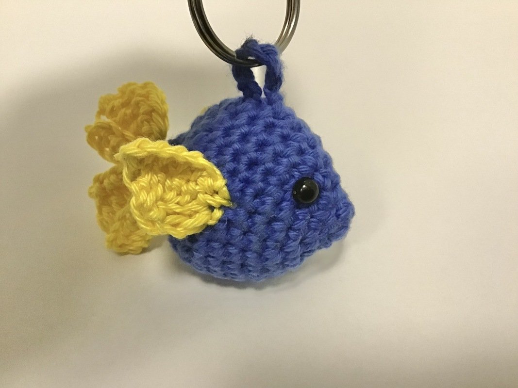 Gehäkelter blauer Fisch mit gelber Flosse an Schlüsselring