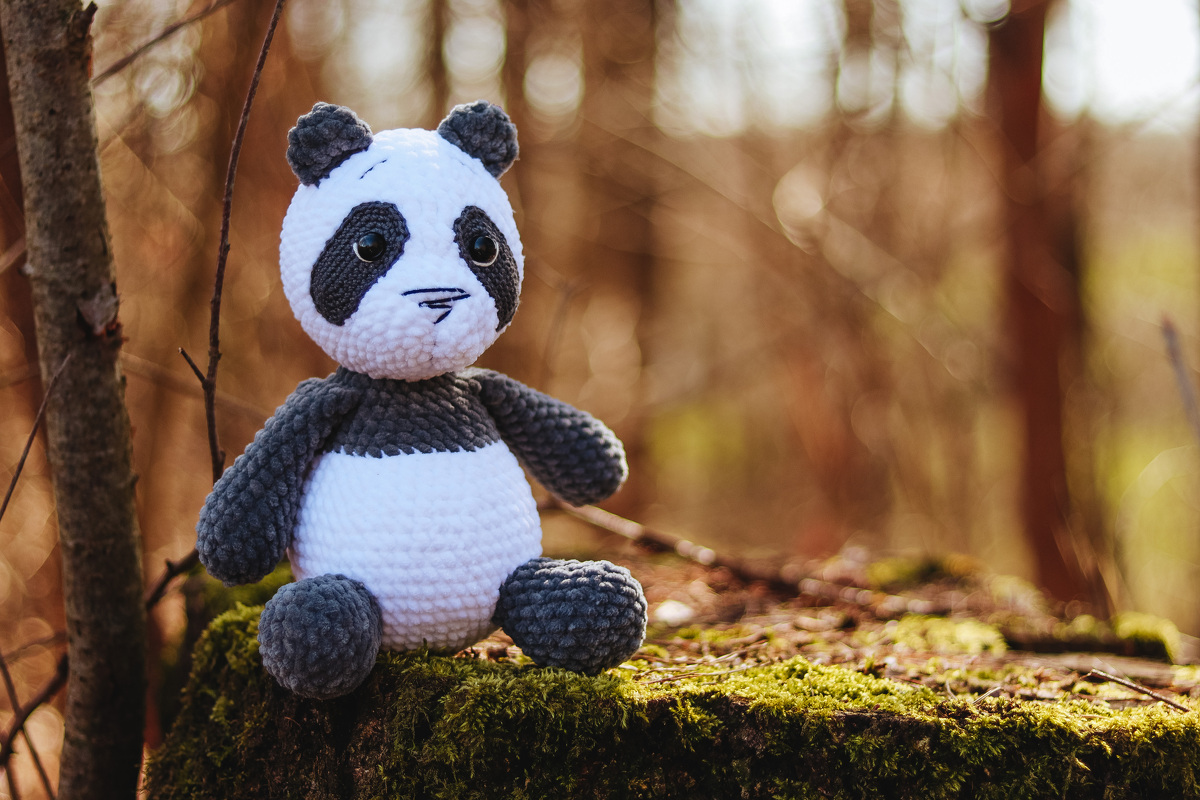 Gehäkeltes Panda-Amigurumi sitzend auf moosigem Baumstumpf im Wald