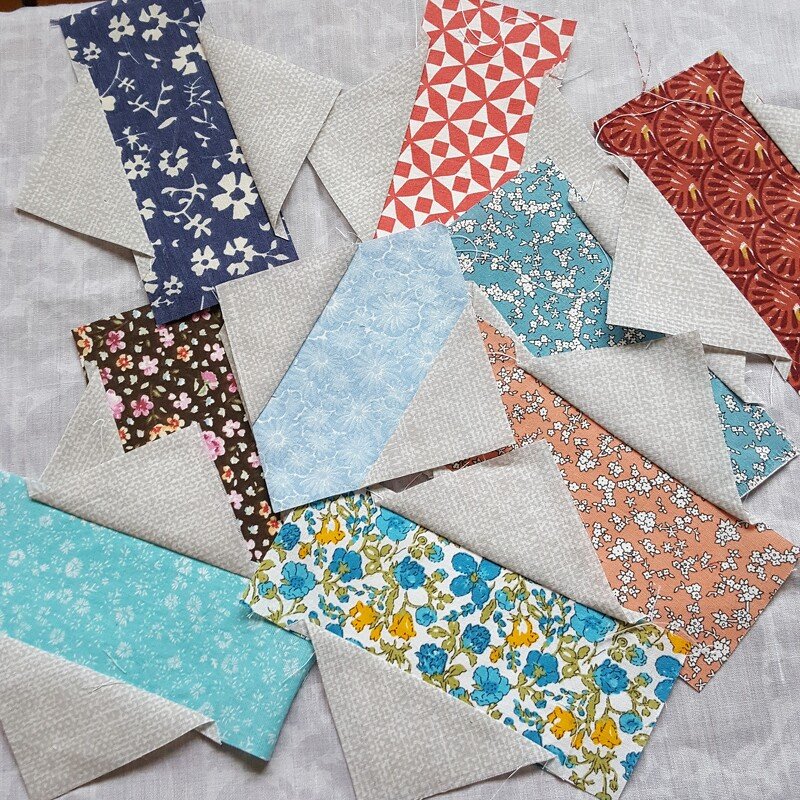 Verschiedene fertig genähte Flying‑Geese‑Quiltblöcke aus gemusterten Stoffstreifen auf hellem Untergrund