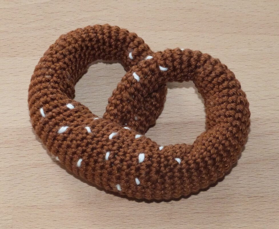Detailaufnahme einer braunen gehäkelten Brezel mit weißen Streuseln auf Holztisch