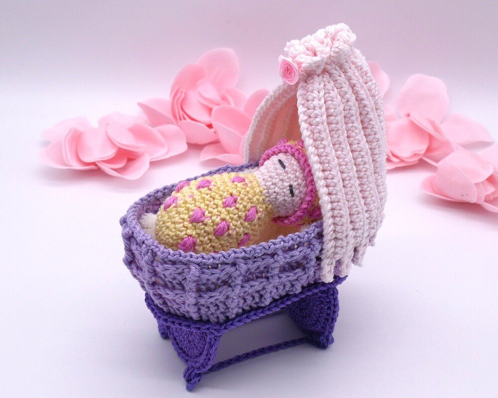 Gehäkelte Babypuppe in lila Wiege mit rosa Haube und gepunkteter Decke
