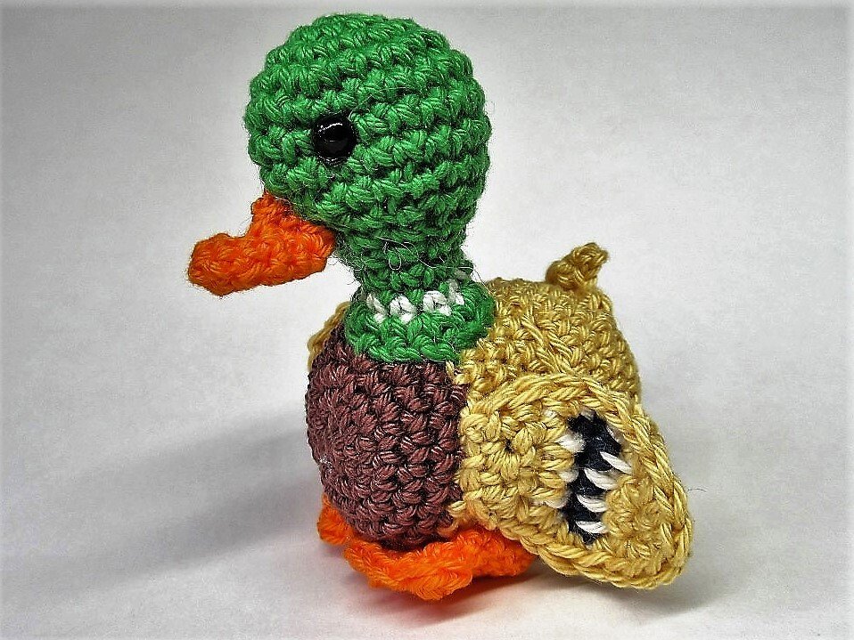 Gehäkelte Amigurumi-Ente mit grünem Kopf, orangem Schnabel und beigefarbenem Flügel