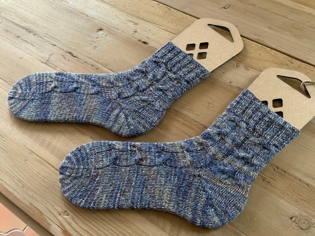 Blau-graue, melierte Socken mit Zopfmuster auf Sockenspannern.