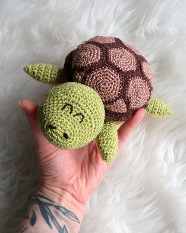 Gehäkelte Amigurumi-Schildkröte (grün/braun) in einer Hand